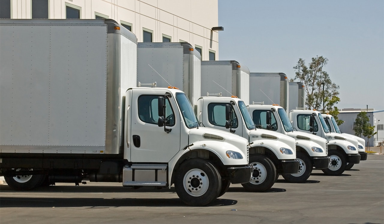 Five trucks lined in a row outside a warehouse.