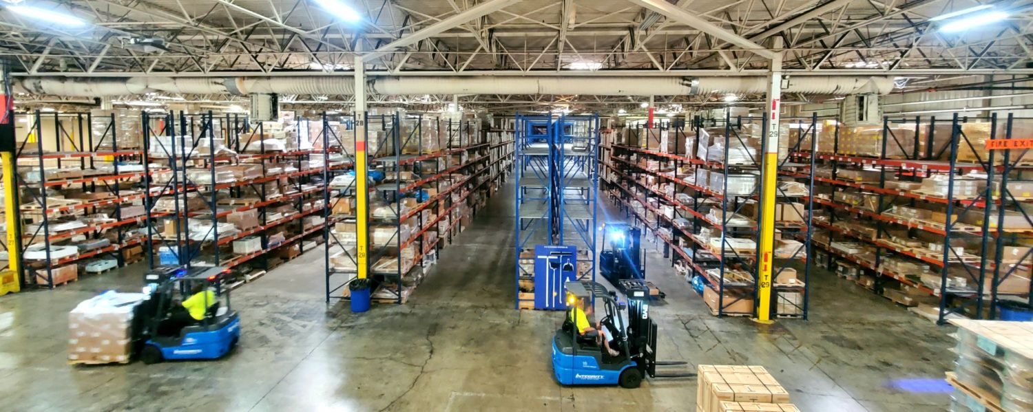 Warehouse with rows of racks and forklifts.